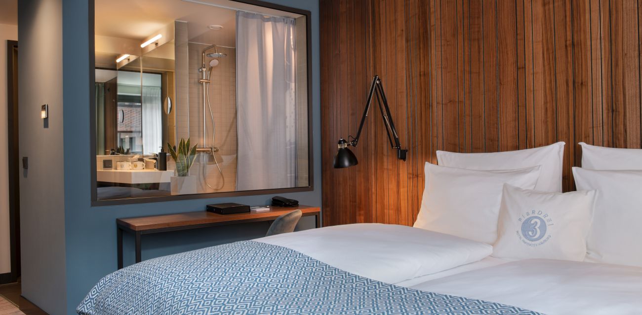 Bed with wooden wall behind it and window with curtain to the bathroom in a room of category MEDIUM PLUS