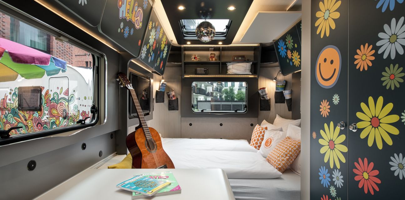 View of the interior of the camper FLOWER Coco with small table, guitar, floral stickers and pulled out bed